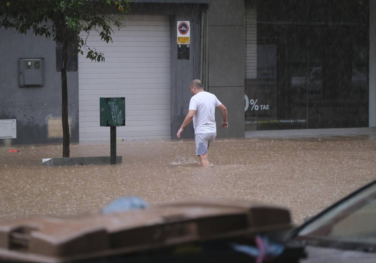 Una hombre intenta cruzar una calle completamente inundada