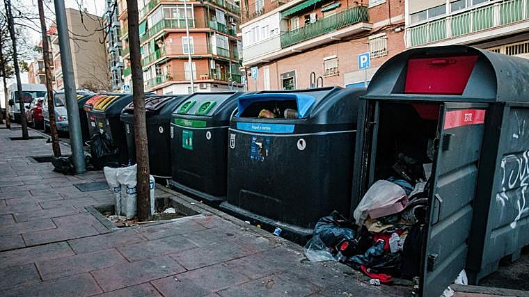 Contenedores de basura llenas de ropa y bolsas de plástico desparramadas en medio de la vía pública