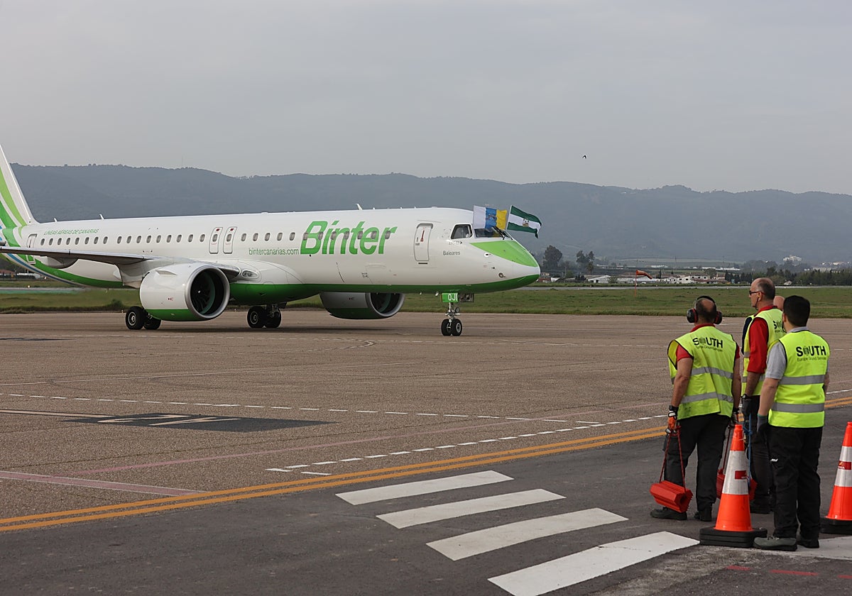 Operarios del aeródromo esperan a la aeronave con las banderas canaria y andaluza en la pista de aterrizaje