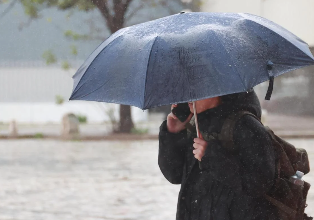 Una mujer se refugia de la lluvia bajo un paraguas en foto de archivo