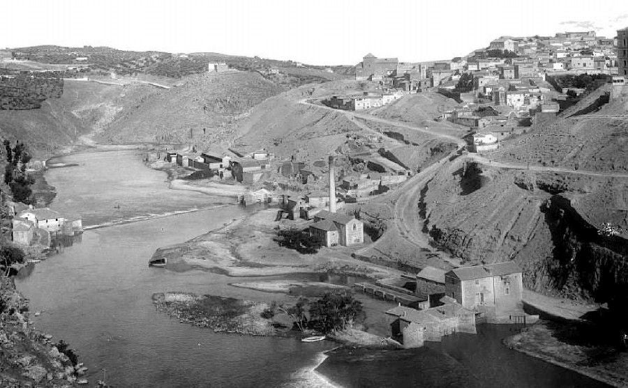 Paraje del Tajo hacia 1910. Abajo, los molinos del Hierro en la presa de Saelices. En el centro, la central de vapor con su chimenea en el arenal de la Incurnia. Al fondo, el azud de Romayla con los batanes de San Sebastián. Archivo Municipal de Toledo
