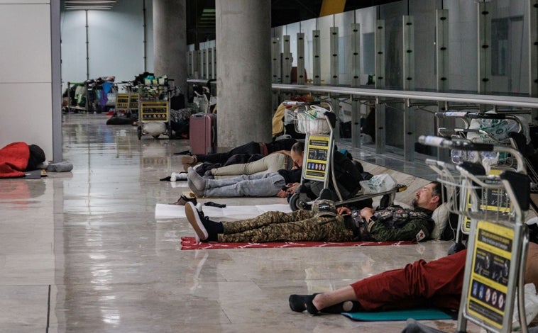Imagen principal - Indigentes pasan la noche en T4 de Barajas la madrugada de ayer; debajo, un trabajador recoge los carritos y una policía nacional en la planta 1