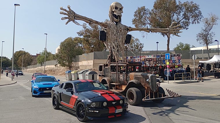Varios Ford Mustang pasan junto a uno de los vehículos de estética 'Mad Max'