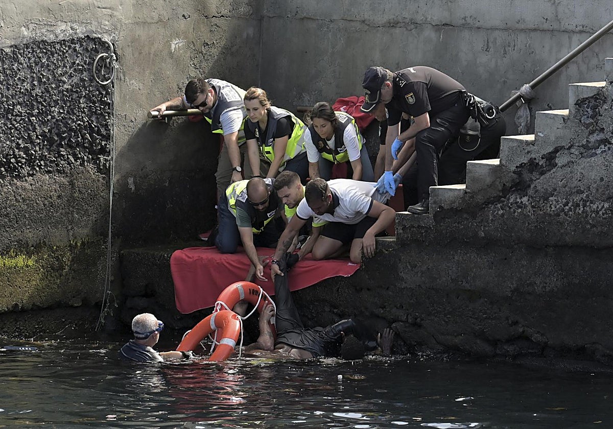 Personal del SUC y cuerpos de seguridad ayudan a un migrante a subir al muelle tras el naufragio del cayuco