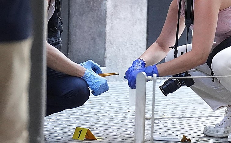 Imagen principal - Arriba, agentes de la Científica localizan una vaina percutida ante el portal donde ha aparecido el cadáver de la víctima. Abajo, acordonando la zona, para la inspección ocular