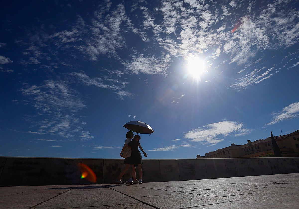 Dos mujeres cruzan el Puente Romano con una sombrilla a pleno sol