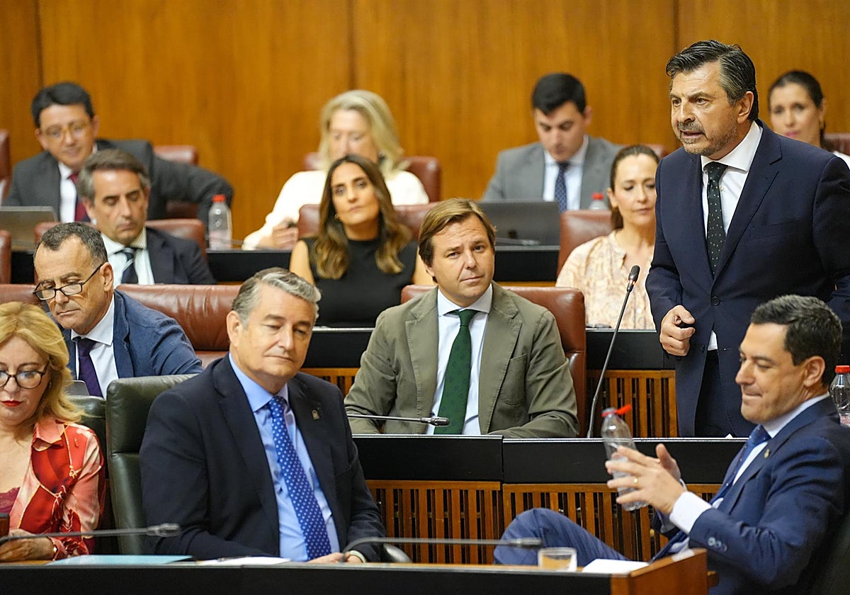 El presidente de la Junta, Juanma Moreno (i), y los consejeros de Presidencia, Antonio Sanz (c); y de Economía, Hacienda y Fondos Europeos, Carolina España (i), en el Pleno del Parlamento mientras habla el portavoz del PP-A, Toni Martín