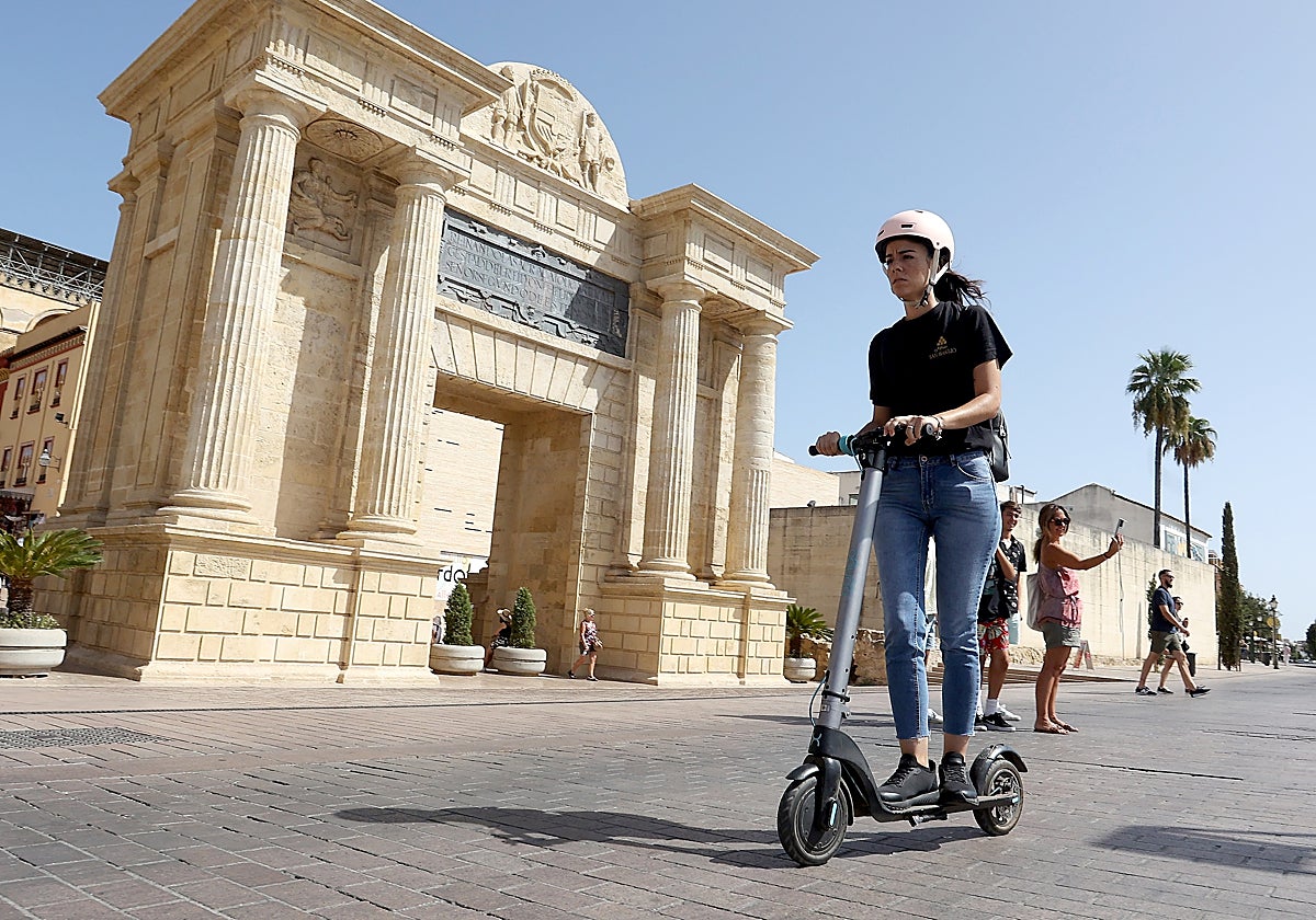 Una joven pasa en patinete, delante de la Puerta del Puente