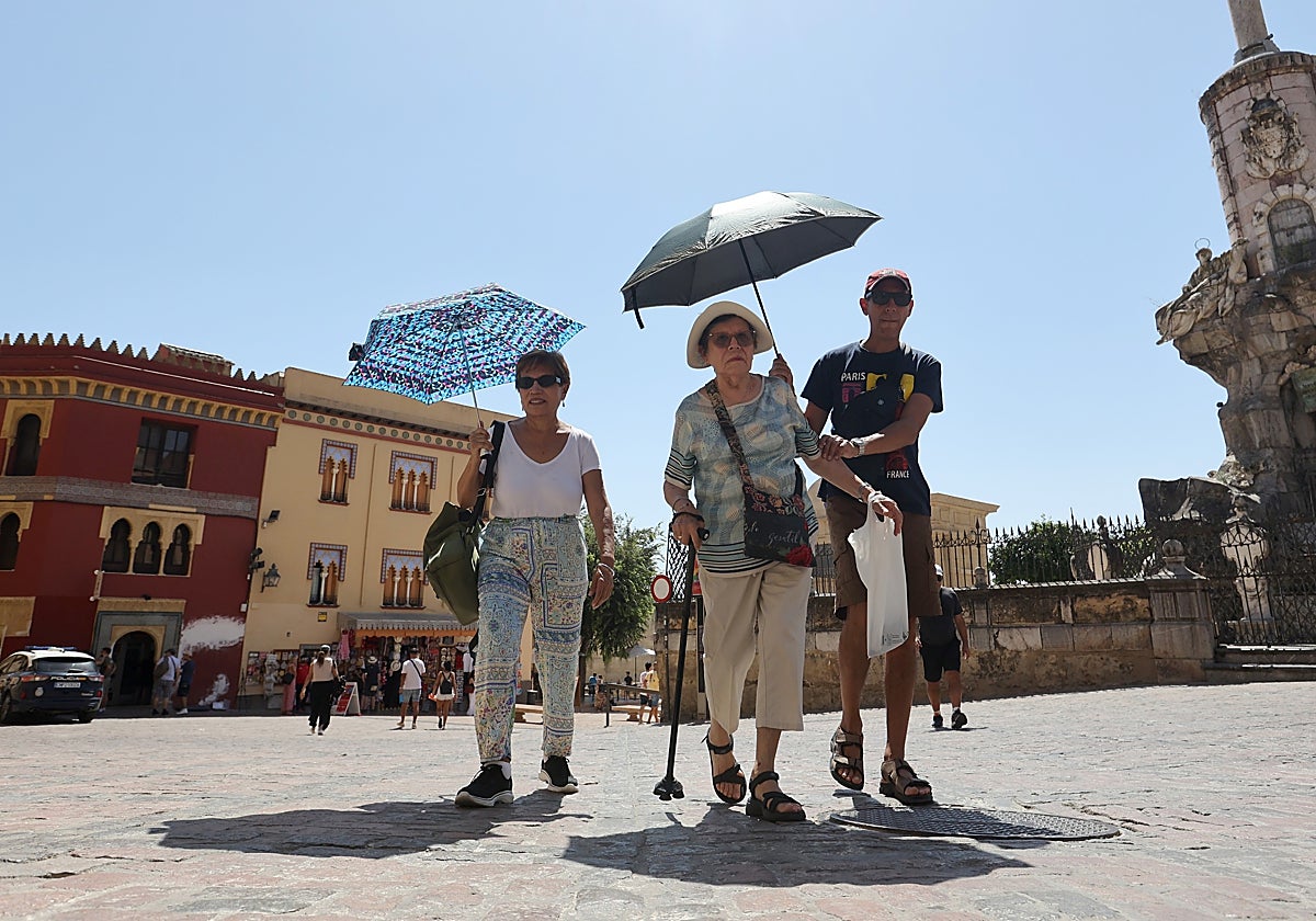 Tres visitantes de Córdoba por la Plaza del Triunfo bajo varios paraguas para soportar el sol