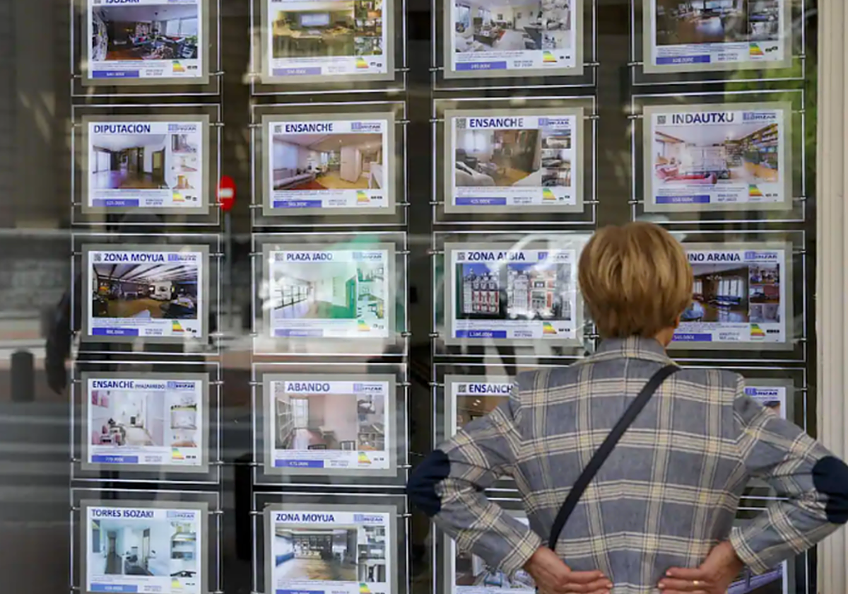 Una mujer mira los carteles de compraventa de vivienda en un escaparate de una inmobiliaria