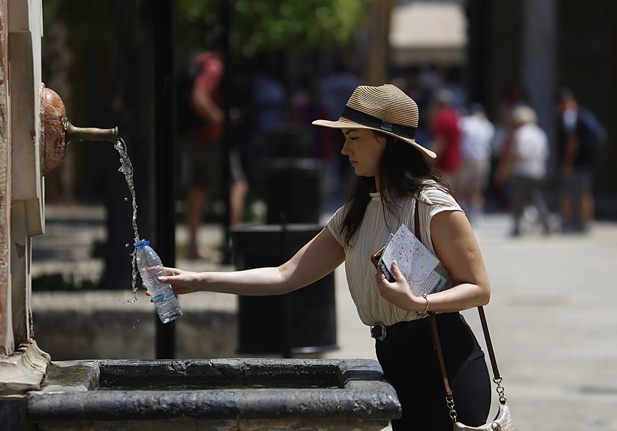 Una joven llena una botella de agua en una fuente en Córdoba