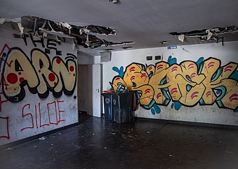 Imagen secundaria 1 - Uno de los pasillos, desprovistos de toda luz, que da acceso a los pisos okupados; en las fotos pequeñas, los grafitis se acumulan en el interior del bloque, y los destrozos y la basura acumulada inundan todas las estancias