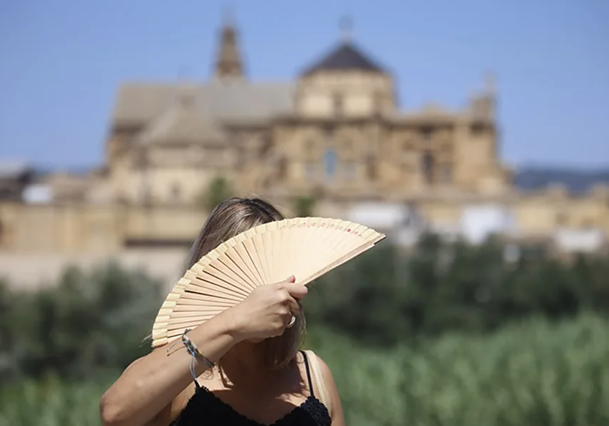 Una mujer se abanica mientras cruza el puente romano de Córdoba durante un jornada de calor