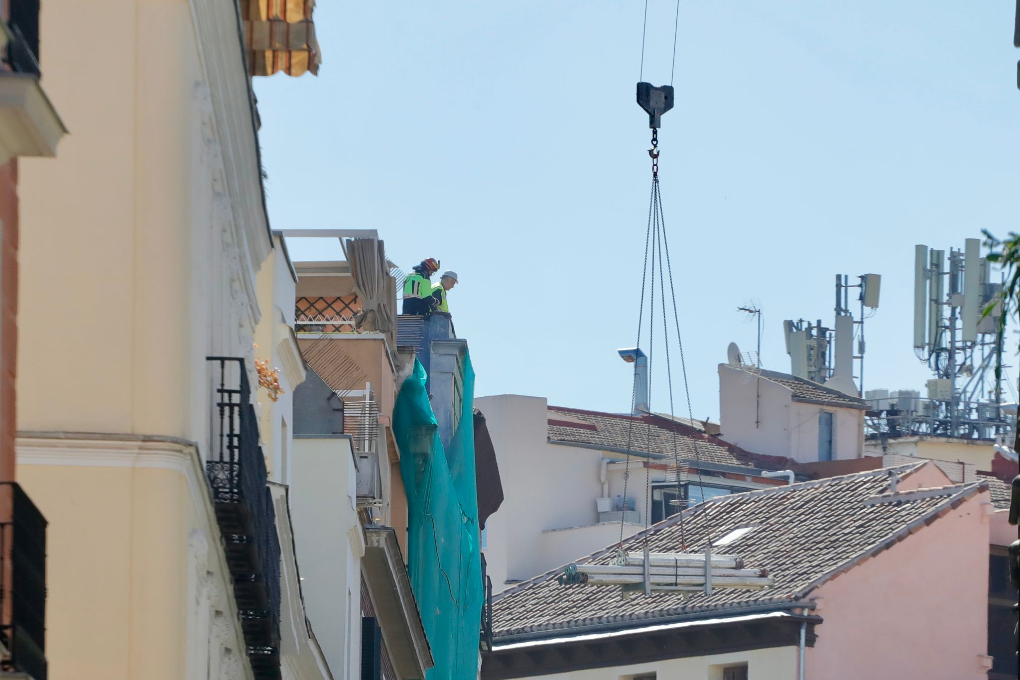 Un bombero y un operario en la fachada del edificio siniestrado, tapada con una tela verde