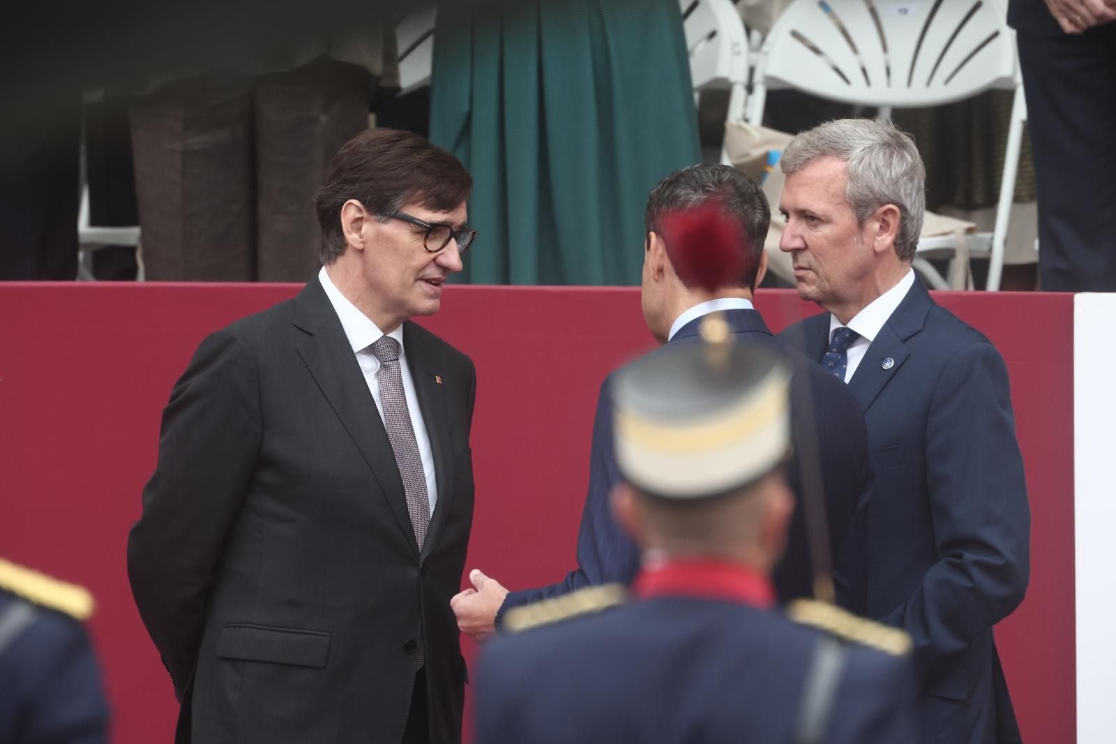 Salvador Illa, departiendo con los presidentes del PP de Andalucía, Juanma Moreno, y Galicia, Alfonso Rueda. Es el segundo año consecutivo que el 'president' está en el desfile del 12-O, tras años de ausencias del gobierno catalán durante su época independentista