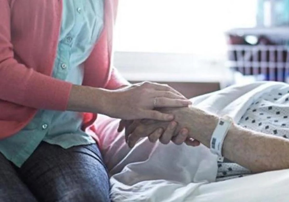 Una mujer le coge la mano a un paciente ingresado en un hospital