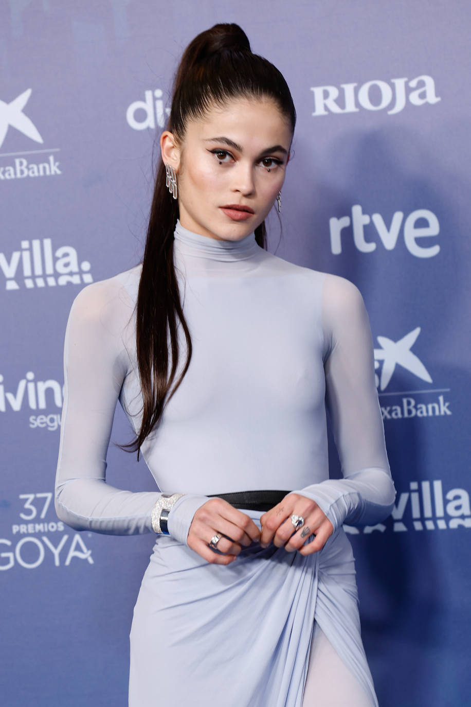 Luna Pamiés, nominada en la categoría de actriz revelación, lució un original 'beauty look' elaborado por Pedro Cedeño con productos de Leonor Greyl para el pelo y de Dior para el maquillaje. La actriz lució una coleta alta extra lisa y extra larga, gracias a extensiones. En la mirada de Luna se refleja el color malva de su vestido gracias a la aplicación de unas partículas de escarcha irisada con reflejos malva. Pedro ha rasgado los ojos con una fina línea de eyeliner negro Diorhow On Stage Liner Matte Black a ras de la hilera de las pestañas superiores. Ha terminado con varias capas de máscara Diorshow Iconic Overcurl en tono 090 Black.