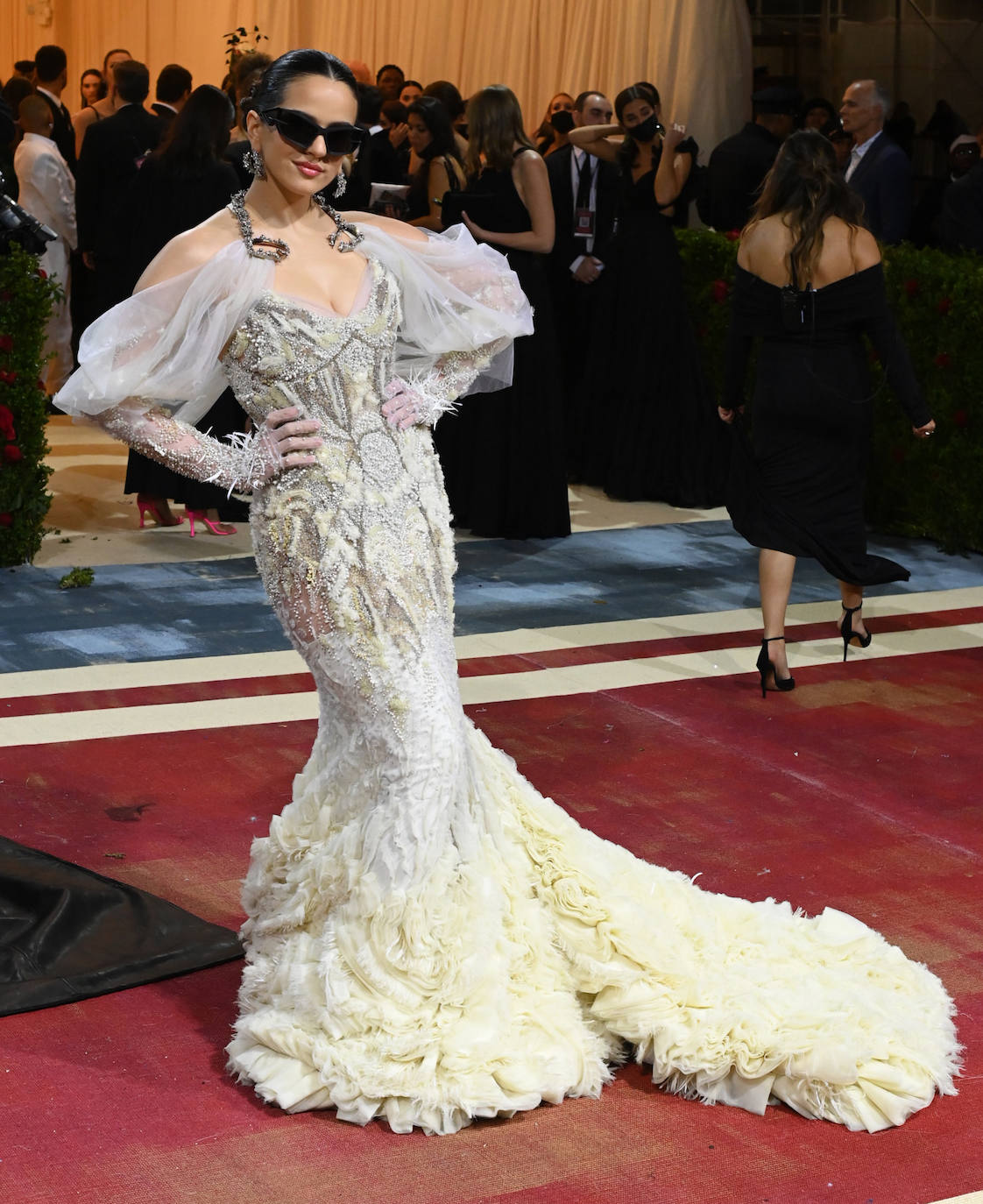 Rosalía en la Gala Met 2022 con vestido blanco roto de Givenchy compuesto por un cuerpo encorsetado de encaje con lentejuelas y transparencias y una larga cola con plumas.