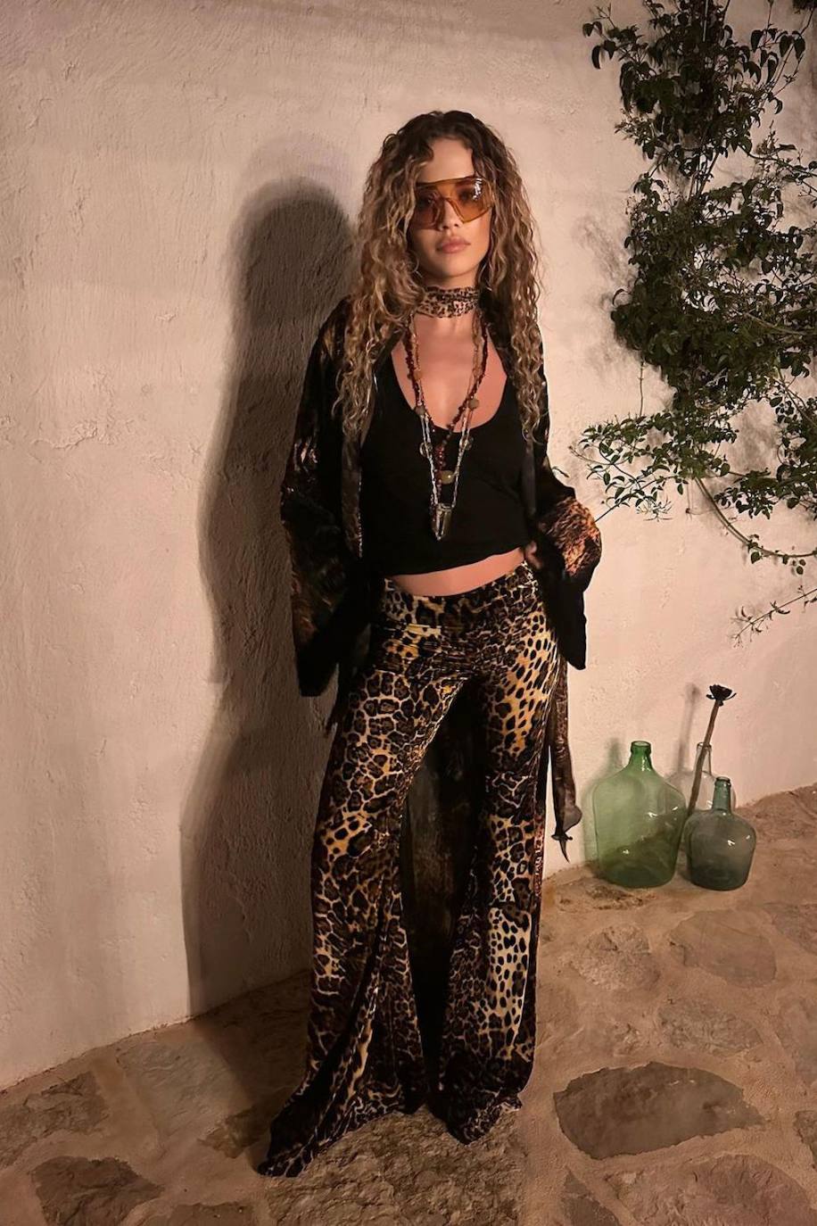 Rita Ora en Ibiza con un look de la Colección Otoño Invierno 23-24 de Roberto Cavalli. El 'outfit' está compuesto por una bata y unos pantalones de terciopelo con estampado 'animal print' y una camiseta negra sin mangas. Además, combinó el conjunto con un bolso de la misma firma. 