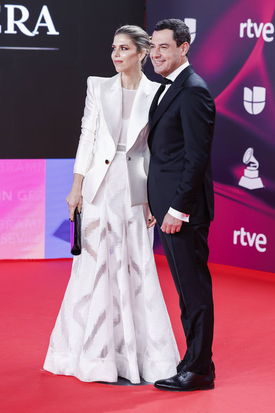 El presidente de la Junta de Andalucía, Juanma Moreno con esmoquin, y su mujer Manuela Villena Lopez con un original look en color blanco, formado por blazer de solapas grandes, falda larga con volumen y top ajustado. 