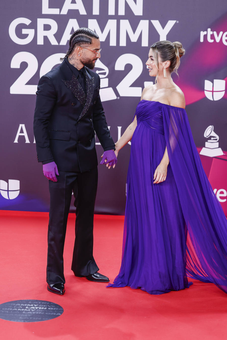 El cantante Maluma de negro con traje satinado y guantes morados. Su novia ha llevado un vestido azul de gasa con capa y escote palabra de honor de Valentino. 