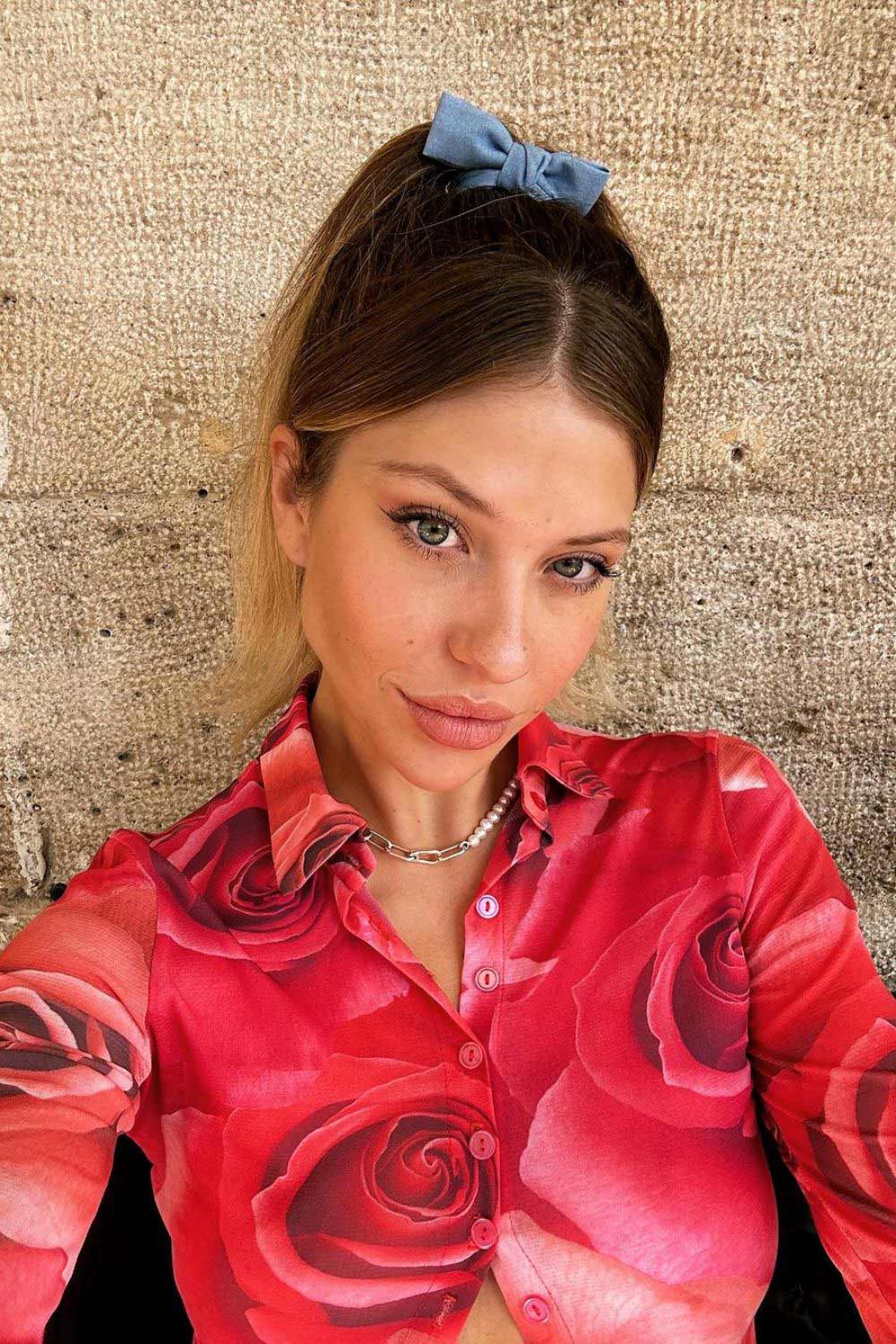 Coleta alta con flequillo suelto y decorada con un lazo. 