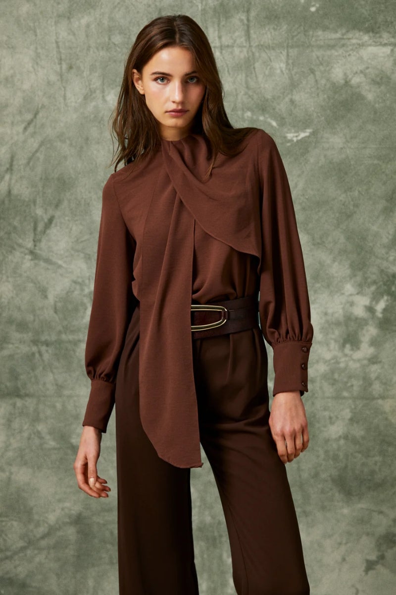 Vogana. Blusa de gasa, modelo ‘Lola’, confeccionada en gasa marrón chocolate con escote a la caja, mangas abullonadas y un volante superpuesto en el cuello como si de un pañuelo se tratase. Perfecta para lucir sin nada o con un cinturón en el caso de que se busque un extra de elegancia. Precio: 129€.