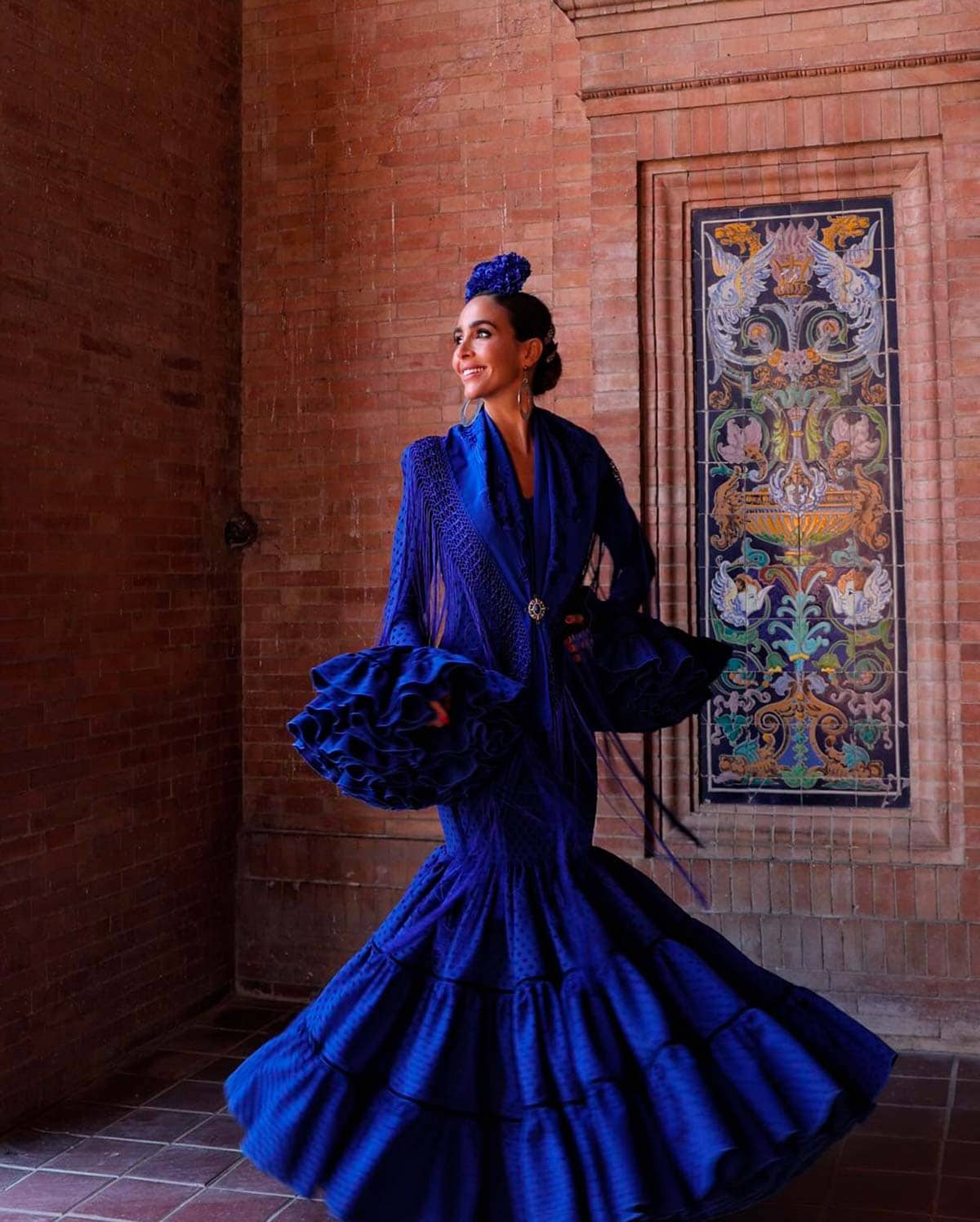 Rocío Osorno ha llevado un vestido en color azul intenso con lunar flocado en terciopelo más oscuro combinado con cintas de terciopelo en el mismo tono. Para el mantón y la flor ha escogido el mismo color.