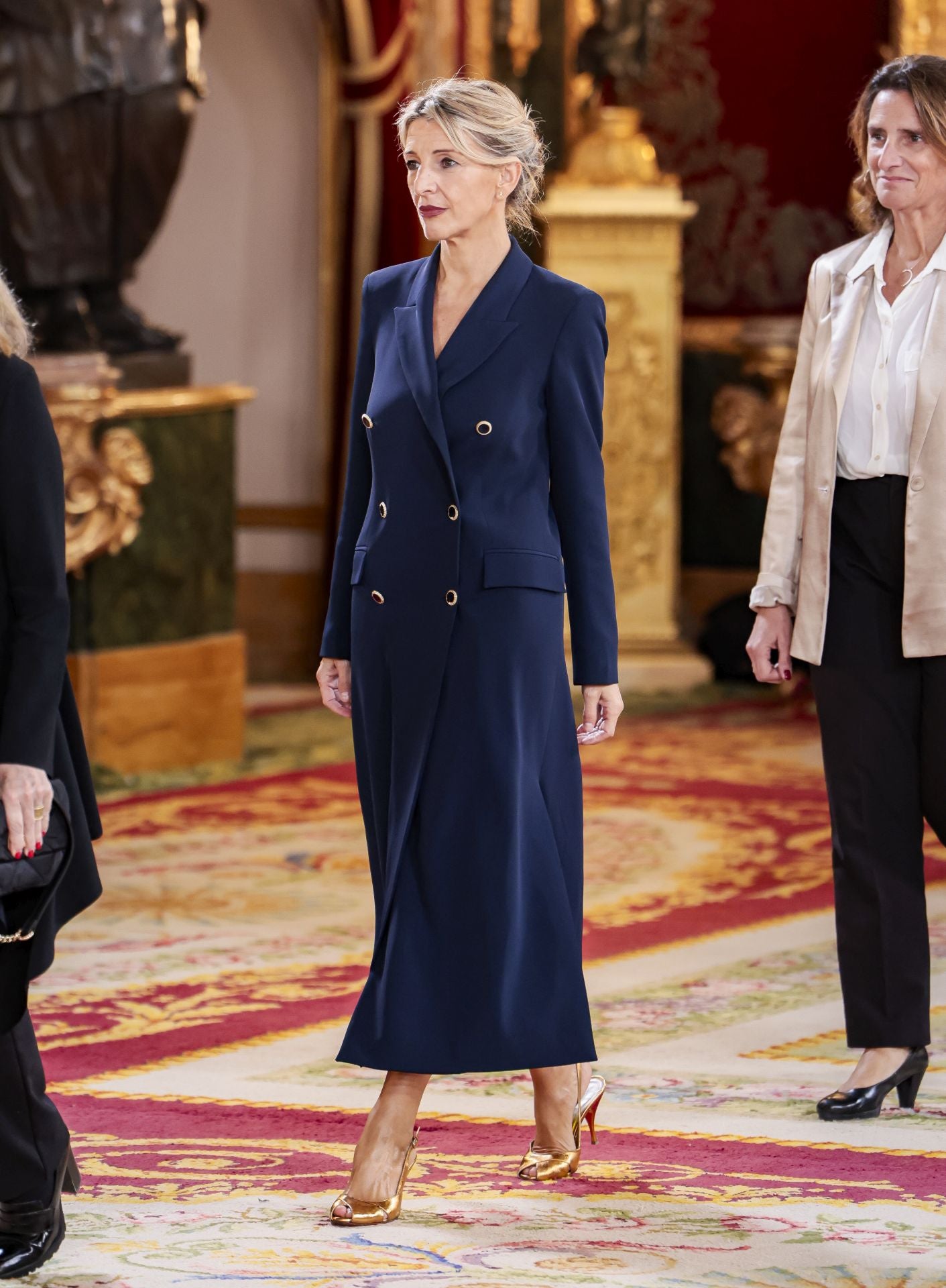 Yolanda Díaz ha apostado por un vestido tipo traje color azul con doble botonadura y detalle de botones con toque dorado. Con cuello tipo sastre y bolsillos con solapa, destaca una amplia abertura en la pierna. La vicepresidenta segunda lo ha combinado con zapatos metalizados dorados.