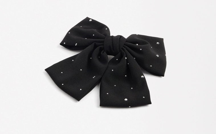 Imagen principal - Lazo con brillos de Parfois (8,99€); Blazer dorada con lazada de Trucco (140€) y pendientes en forma de lazo de El Corte Inglés (9,99€)