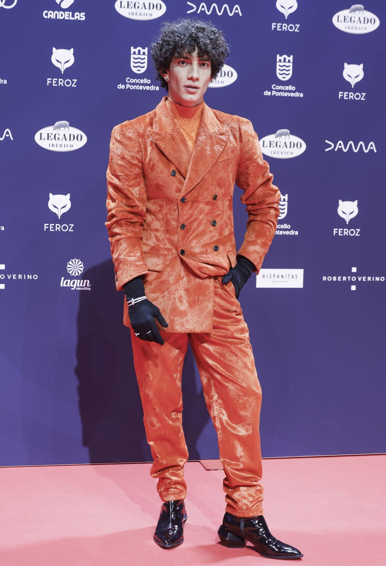 El actor Jorge López ha apostado por un llamativo look con traje de chaqueta de doble botonadura en color naranja que ha combinado con jersey de cuello alto al tono y llamativos guantes negros a contraste con joyas sobrepuestas. 