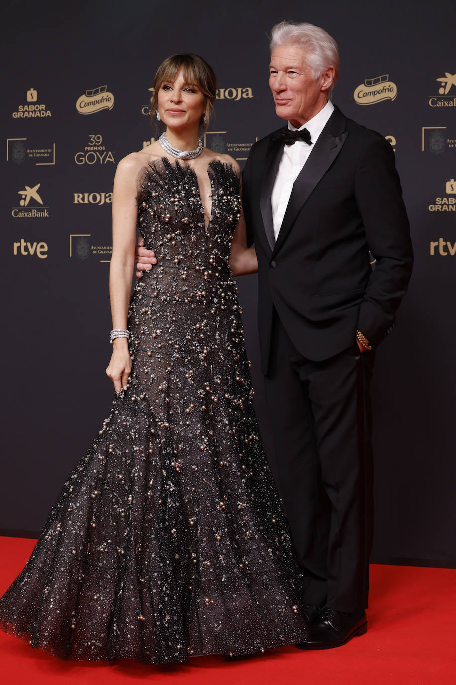 Richard y Alejandra Gere vistieron de Georgio Armani. El actor, siempre elegante, optó por un esmoquin clásico. Su mujer llevó un vestido de noche de tul negro de Giorgio Armani Privé con lunares de lamé, bordado con perlas y cristales. Además, la española lució joyas de Bulgari, zapatos de Aquazzura y clutch de Roger Vivier.