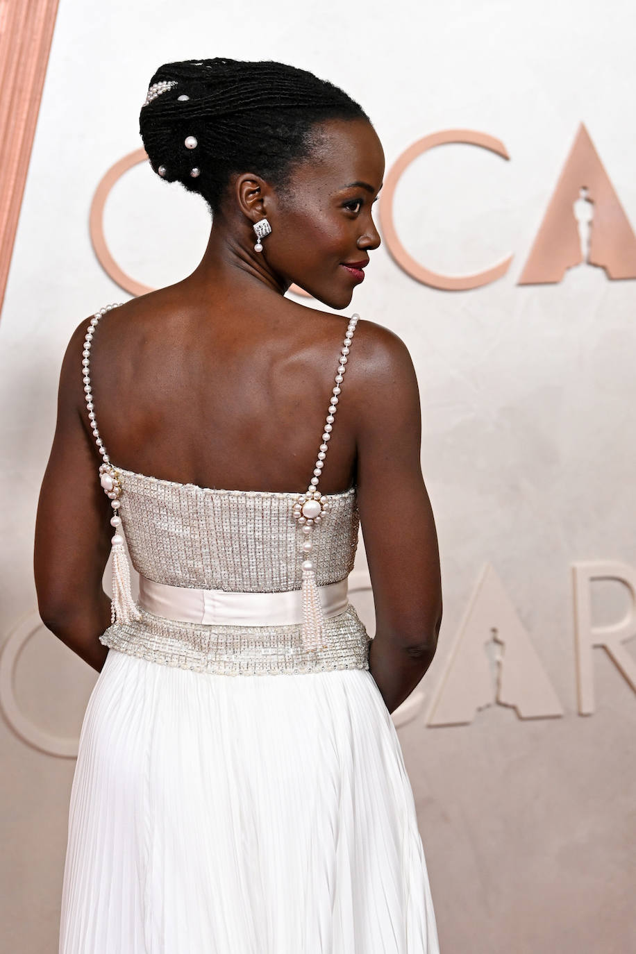Lupita Nyong'o recogió su melena en un moño que adornó con perlas. Completó el look con un bonito maquillaje con sombras azules. 