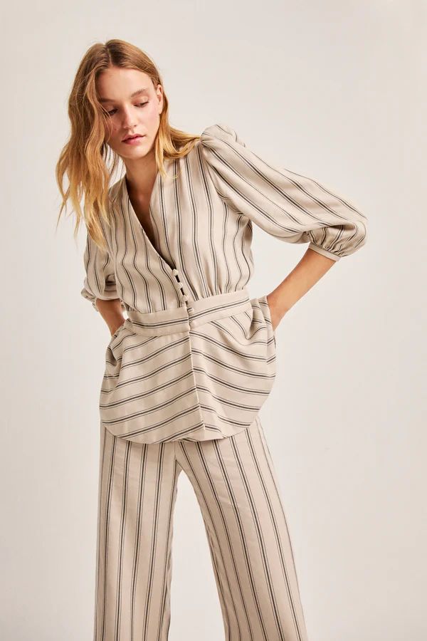 El conjunto 'Greta Beige' de Vogana está compuesto por una chaqueta cruzada de corte peplum con escote en uve y manga tres cuartos abullonada. El pantalón con pernera recta y tiro alto cuenta con el mismo estampado a rayas con fonde beige. Precio: chaqueta 189€ y pantalón 129€