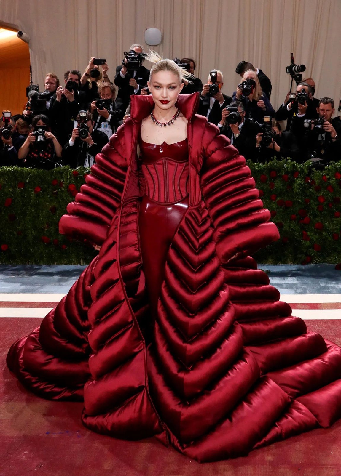 De Versace, Gigi Hadid pisó la alfombra roja de la Gala Met de 2022 con un conjunto burdeos formado por un mono con pantalones de vinilo ajustados, corsé y un amplio y voluminoso abrigo