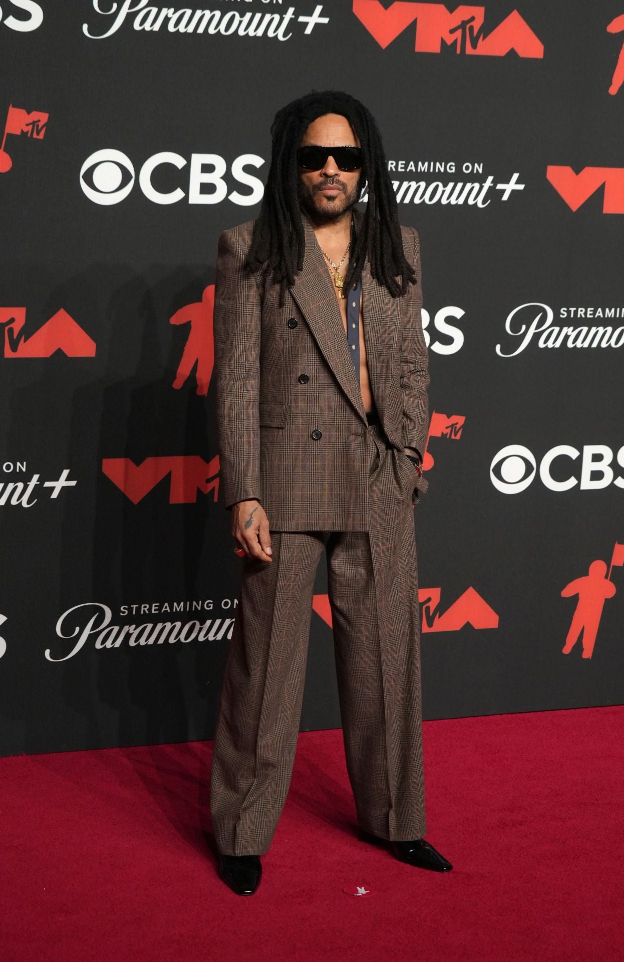 Lenny Kravitz, con traje marrón con corbata a modo de pañuelo y sin camisa. 