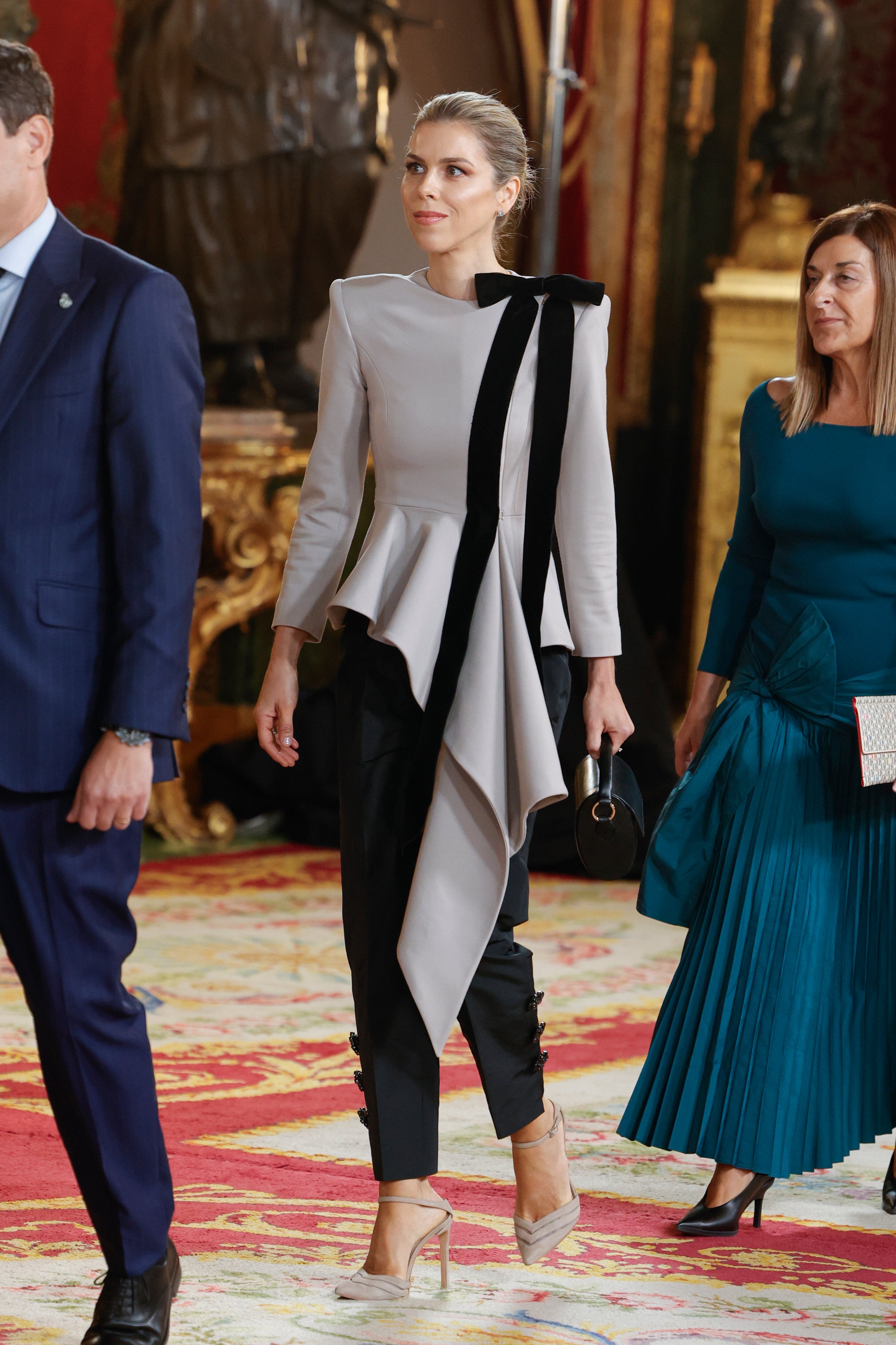 Manuela Villena, mujer del presidente de la Junta de Andalucía, Juanma Moreno Bonilla, se ha decantado una vez más po run diseño de IQ Collection. Se trata de uno de los looks más vistosos de la celebración, compuesto por una llamativa chaqueta con el bajo peplum con lazada, y un pantalón de seda decorado con botones joya. Se trata concretamente de los modelos Celestina y Narváez de la firma de la diseñadora jerezana Inés Domecq