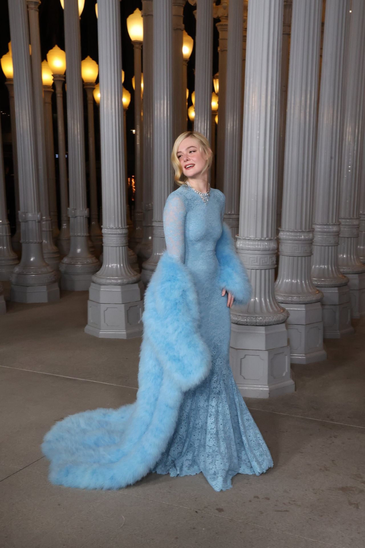 Elle Fanning con vestido de encaje azul de manga larga y un abrigo de pelo del mismo tono, también de Gucci.