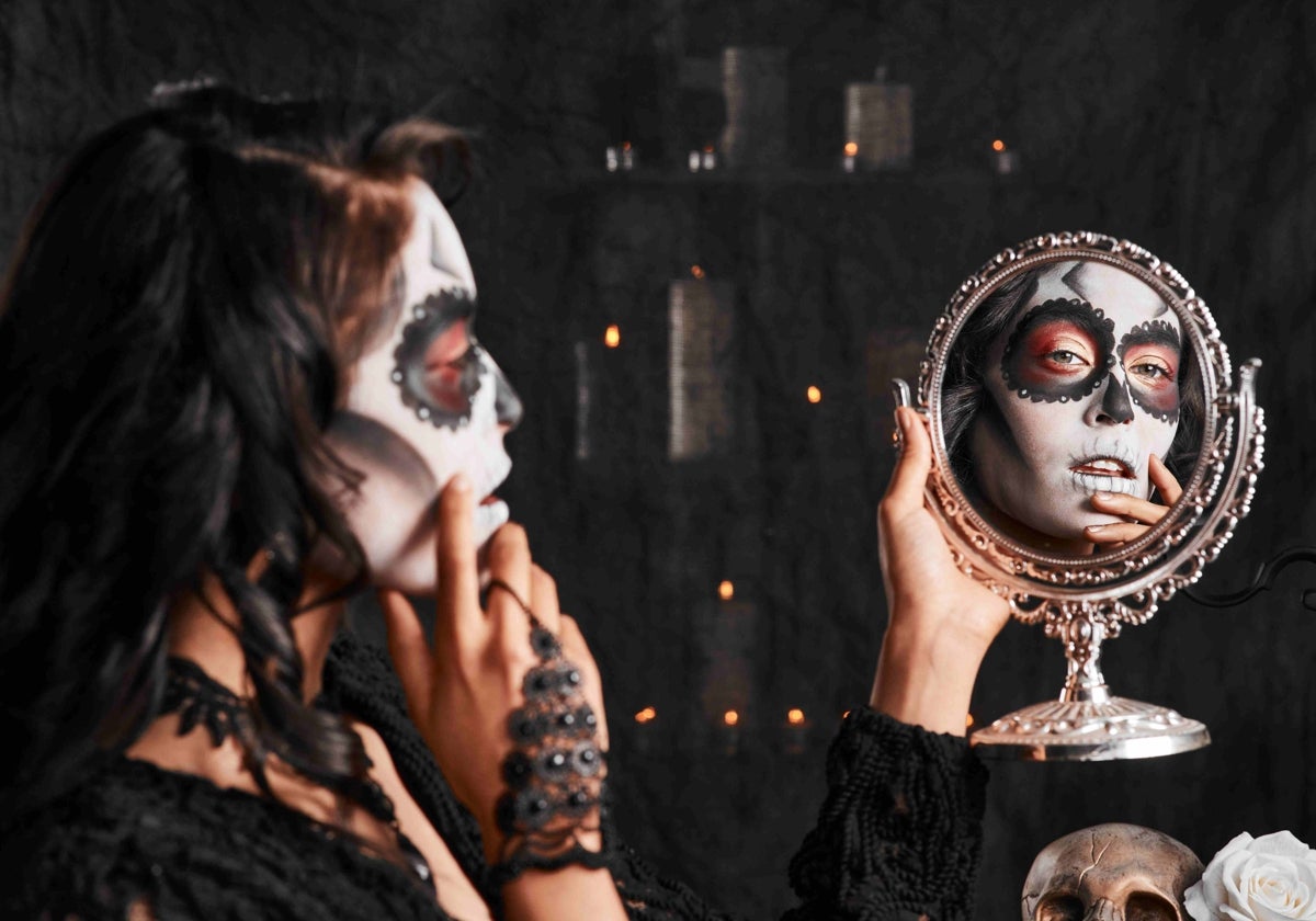 Una chica se mira al espejo para comprobar su maquillaje de Catrina