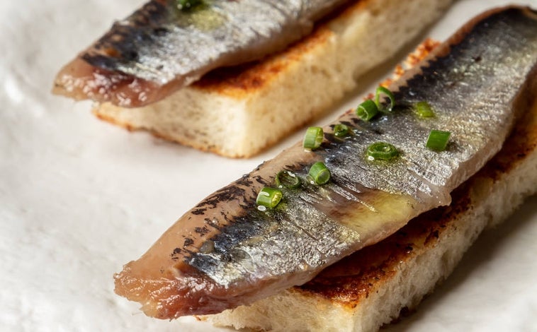 Imagen principal - Sobre estas líneas, las sardinas ahumadas sobre pan de brioche. Abajo, a la izquierda las mesas de Madrí Madre bordeando los ventanales de la taberna. A la derecha, el sándwich Tintín