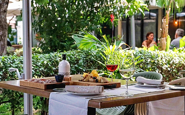 Imagen principal - Sobre estas líneas, la terraza de El Rincón de Vespok, en la urbanización Puerta de Hierro de Madrid. Abajo, alguna de sus propuestas de picoteo y la tarta de quesos ahumados para dos que hornean al momento
