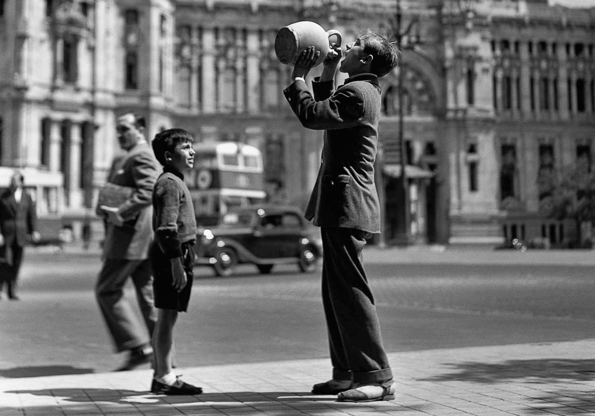 Un adolescente bebe de un botijo frente al Palacio de Comunicaciones de Madrid, en 1952