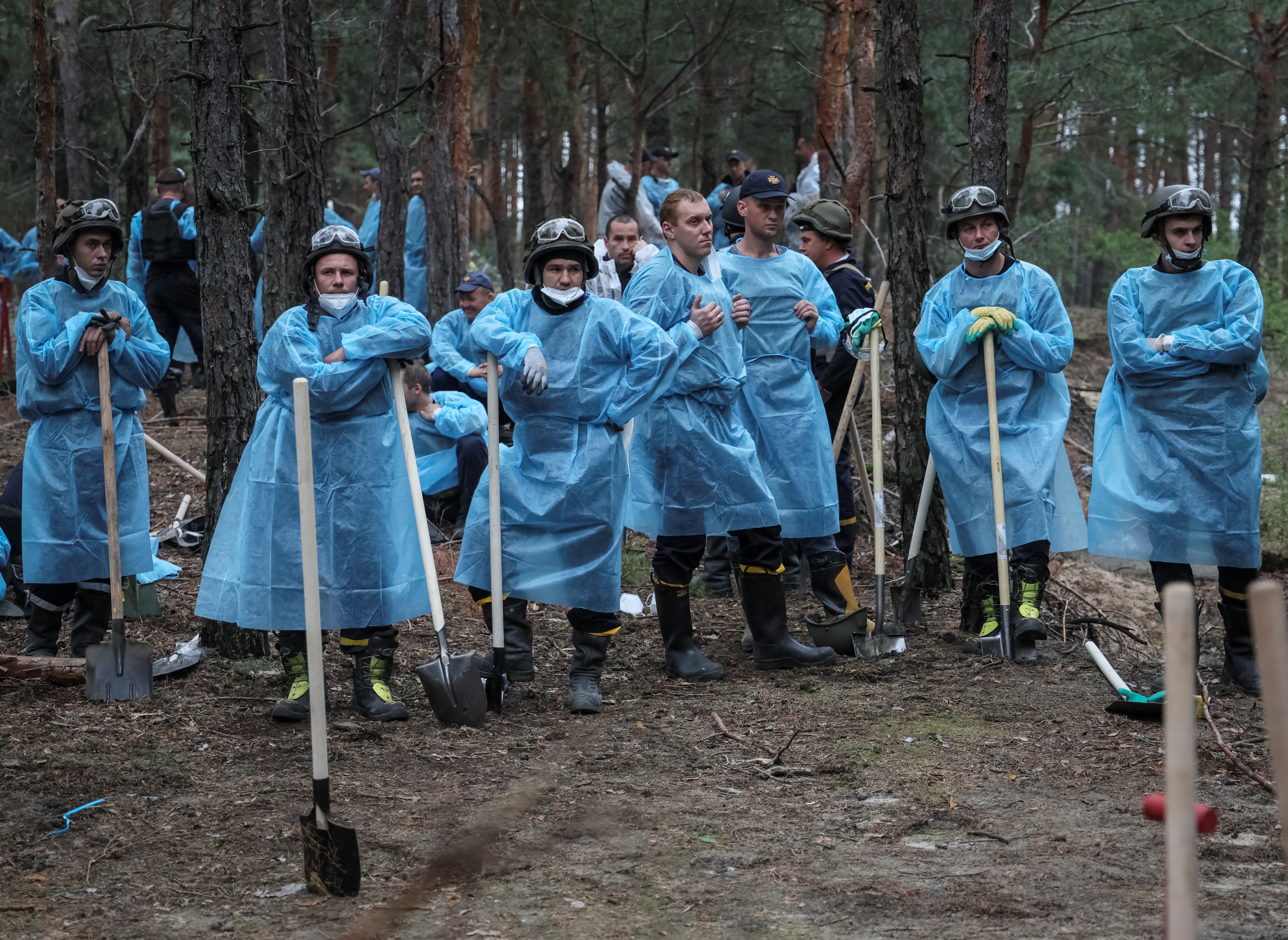 En imagen, voluntarios de los servicios de Emergencia ucranianos esperan a proceder la exhumación de los cuerpos del bosque de Izium