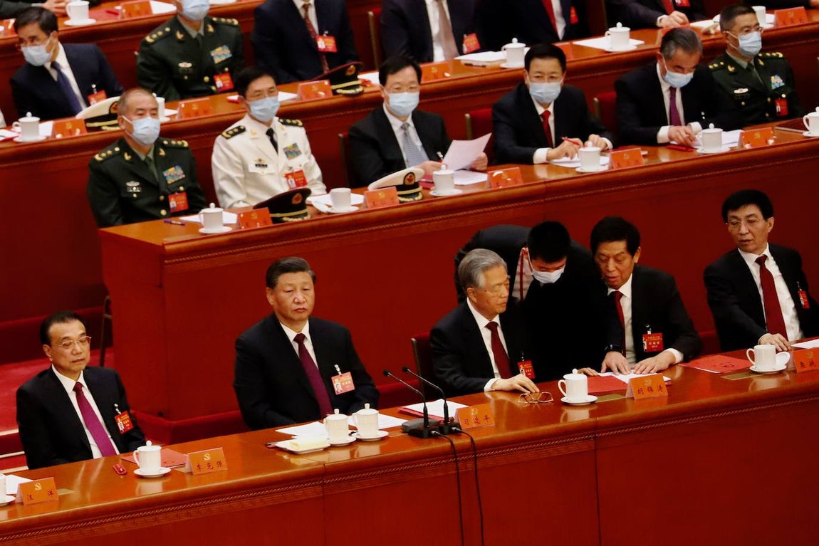 El bedel le comunica a Hu Jintao que debe abandonar la sala mientras Xi Jinping, impertérrito, mira ausente al frente.