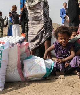 Imagen secundaria 2 - Campamento de desplazados en Yemen, al que la ONG lleva depósitos de agua, el bien más escaso del país. Debajo, un grupo de niñas come su desayuno y otro niño del campo posa con los sacos de provisiones