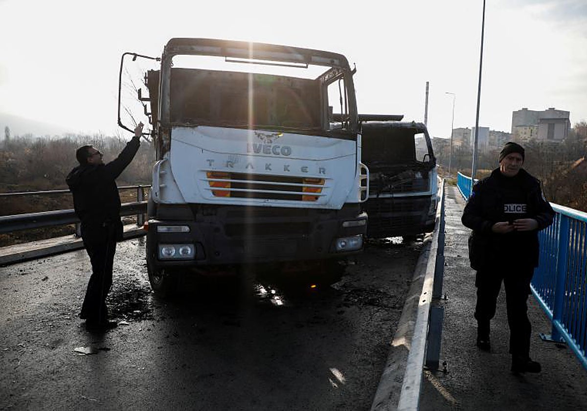 Agentes kosovares revisan camiones quemados que bloquean una carretera en Mitrovica, dividida étnicamente