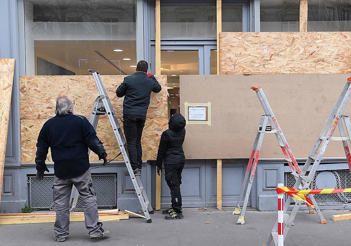 Un grupo de trabajadores protege con paneles de madera un escaparate de París