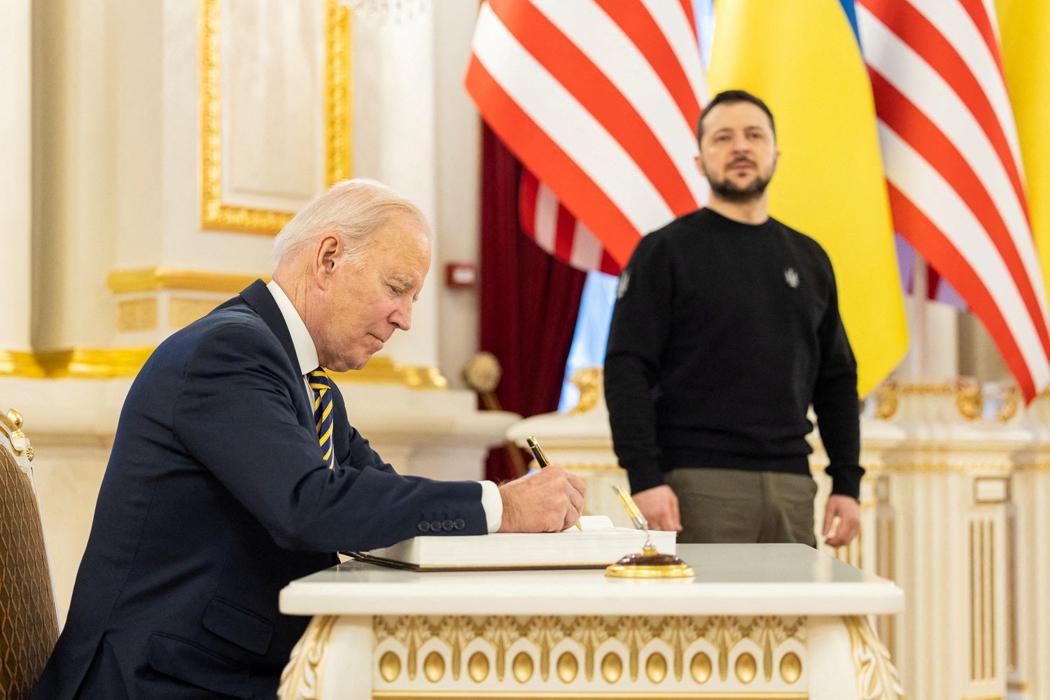 El presidente Biden deja su firma en el libro de Zelenski ante su atenta mirada.
