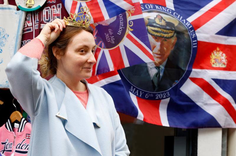 Una chica posa con una corona de plástico junto a un pañuelo con la fotografía de Carlos III en Windsor.