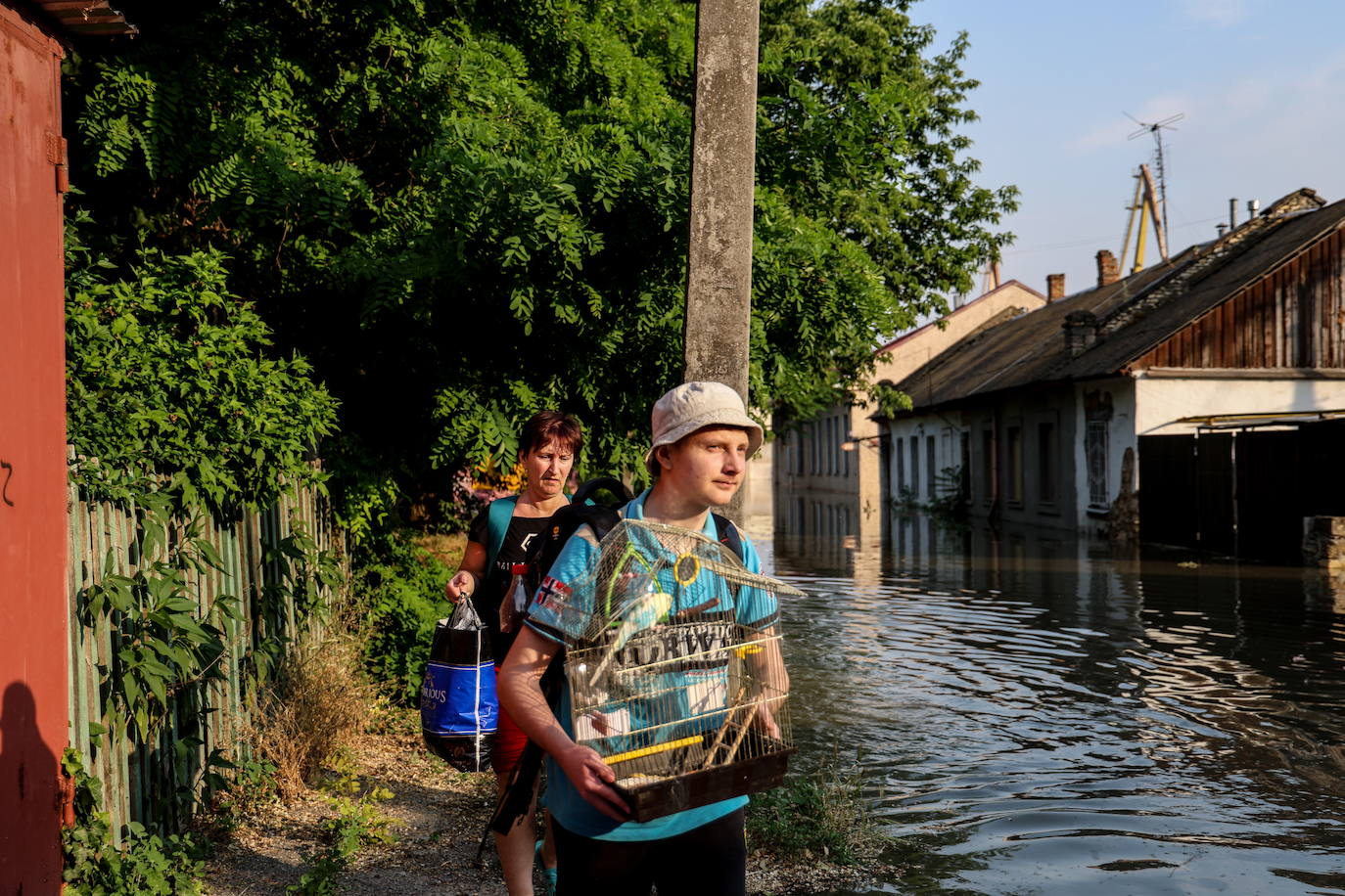 Un joven lleva una jaula con su pájaro mientras evacúa de su casa en una calle inundada de Kherson, Ucrania